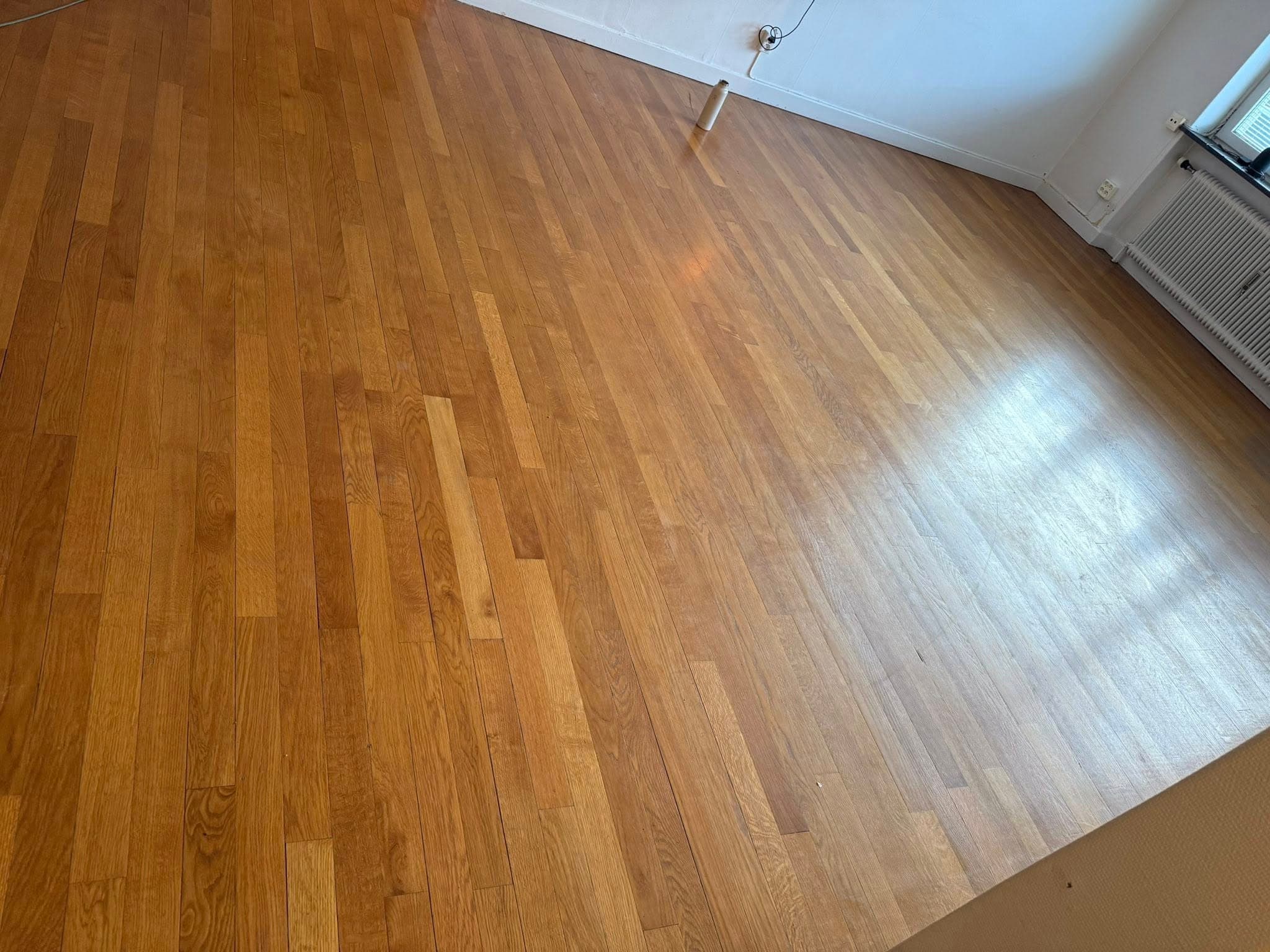 Slitet parkettgolv i vardagsrum före slipning: matt yta och ojämn ton mellan brädor.