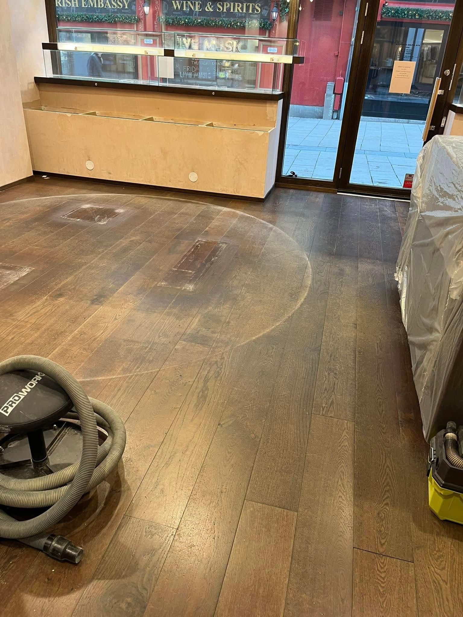 Slitet trägolv i butikslokal före slipning: repor och matt yta.